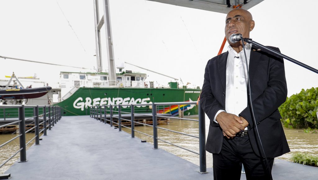 fotografia REGISTRA O REITOR DA ufpa, Gilmar Pereira DA Silva, FALANDO AO MICROFONE. Ao FUNDO, É POSSÍVEL IDENTIFICAR uma grande embarcação na cor verde, identificada com Greenpeace.