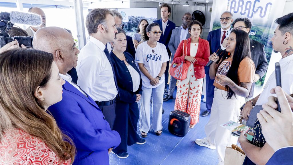 Fotografia registra um grupo de pessoas observando uma mulher falar ao microfone.