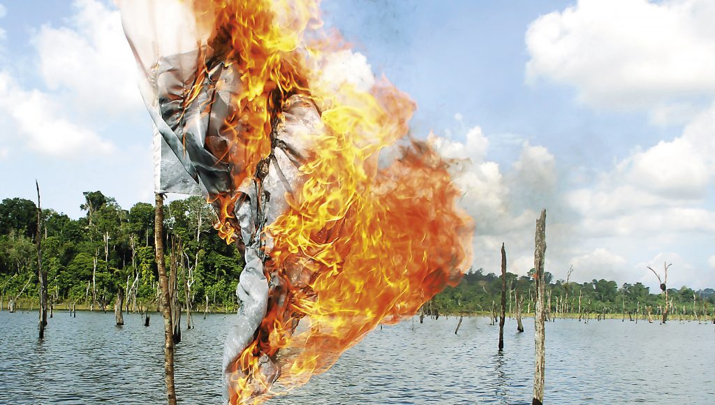 Fotografia registra algo semelhante a uma bandeira, pegando fogo, em um mastro dentro de um rio.
