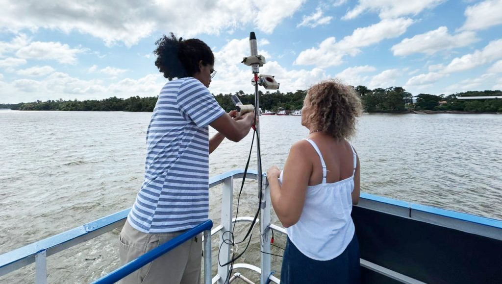 Fotografia registra duas pessoas manuseando uma ferramenta em direção ao rio.