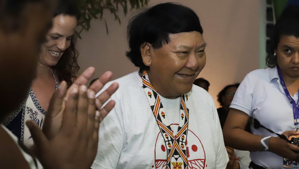 Fotografia registra o indígena Davi Kopenawa. Ele sorri. 