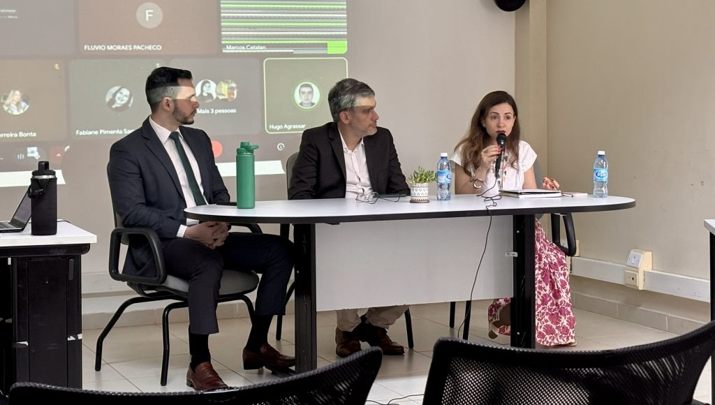Fotografia registra a mesa de um evento, nela estão três pessoas, entre elas, a vice-reitora da UFPA, Loiane Prado Verbicaro.