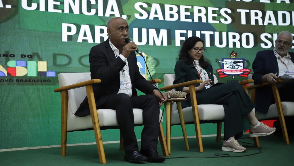 Fotografia destaca o reitor da UFPA, Gilmar Pereira da Silva, falando ao microfone em uma apresentação. Ele ´observado por um homem que está ao seu lado.