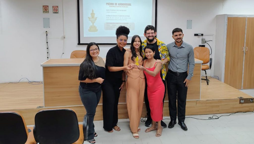 Fotografia registra um grupo de jovens segurando um troféu. Todos sorriem e olham pra foto.