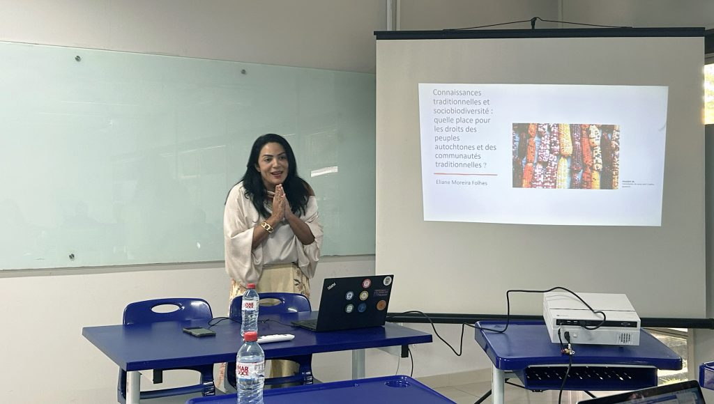 Fotyografia registra uma mulher, falando ao microfone, ao lado de uma projeção.