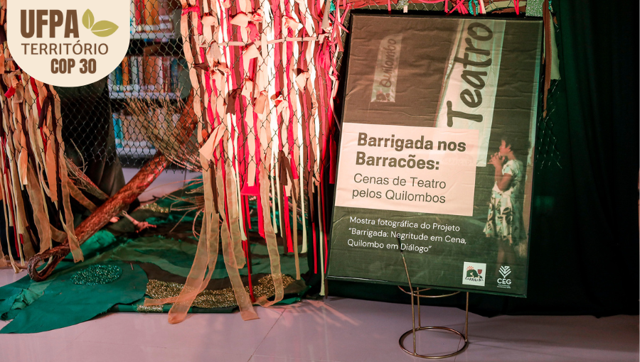 Fotografia registra um banner de uma mostra fotográfica do projeto "Barrigada: negritude em Cena, Quilombo e diálogo". O banner tem a imagem de uma criança olhando para um teatro. Sobre a foto, um selo identifica: UFPA TERRITÓRIO DA COP.