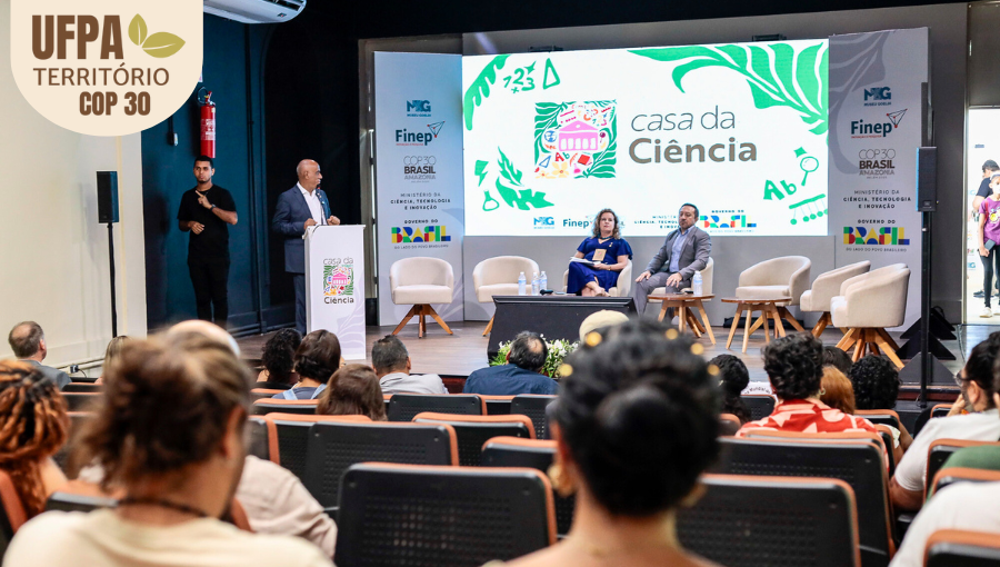 Fotografia registra um palco. Na lateral esquerdo, o reitor da UFPA, fala ao microfone de um púlpito. No centro do palco, uma mulher e um homem estão sentados em cadeiras dispostas em um semi-círculo. Ao fundo, um telão destaca a informação: CASA DA CIÊNCIA. Sobre a foto, um selo identifica: UFPA TERRITÓRIO DA COP.