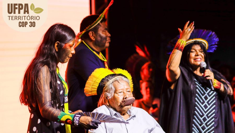 Fotografia registra quatro pessoas com acessórios indígenas. Ao meio, o líder indígena Raoni Metuktire, ao seu lado, falando ao microfone, a Ministra dos Povos Indígenas, Sônia Guajajara. Sobre a foto, um selo identifica: UFPA TERRITÓRIO DA COP.