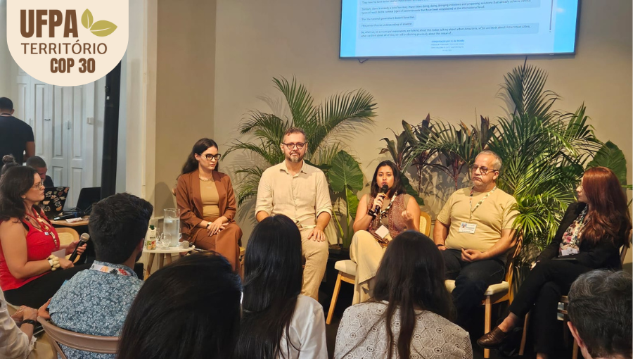 Fotografia de uma grupo de pessoas apresentando um painel. Sobre a foto, um selo identifica: UFPA TERRITÓRIO DA COP.