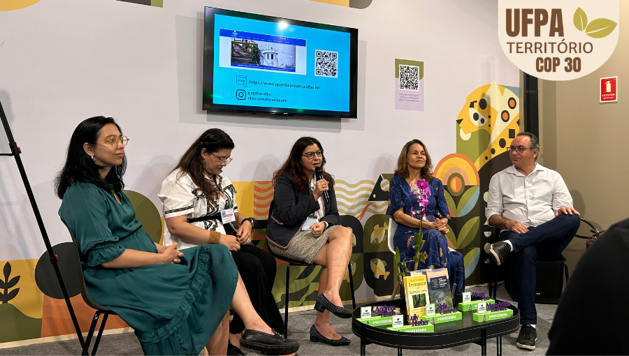Fotografia registra um grupo formado por cinco pessoas, quatro mulheres e um homem, sentado em cadeiras dispostas em frente a um TV com projeção. Uma mulher fala ao microfone. Sobre a foto, um selo identifica: UFPA TERRITÓRIO DA COP.