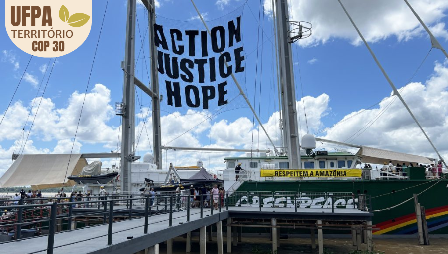Fotografia registra uma grande embarcação ancorada em um pier. Uma tela, no topo da embarcação, destaca a mensagem: ACTION JUSTICE HOPE.