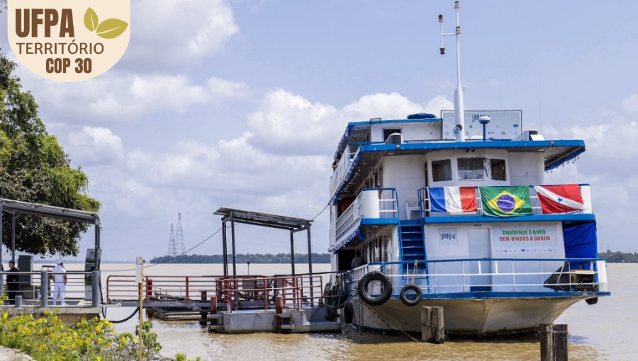 Fotografia registra uma grande embarcação, nas cores branco e azul, atracada em um porto. Na frente da embarcação, estão expostas as bandeiras da França, do Brasil e do Pará. Abaixo das bandeiras, duas placas: IARUÇU e BIENVENUE À BORD - BEM VINDOS À BORDO. Sobre a foto, um selo identifica: UFPA TERRITÓRIO DA COP.