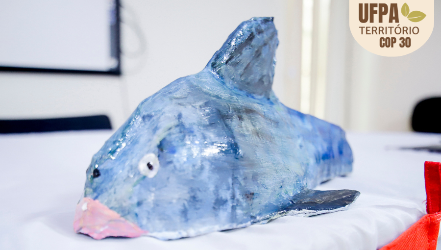 Fotografia registra a reprodução de um peixe em material plástico. Sobre a foto, um selo identifica: UFPA TERRITÓRIO DA COP.