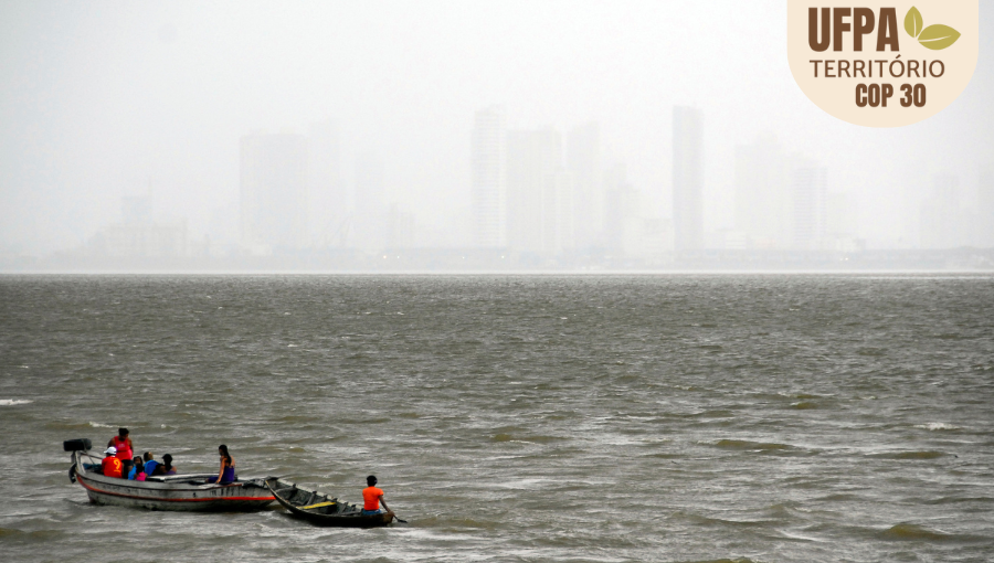 Fotografia registra duas pequenas canoas em um grande rio. Ao fundo, é possível identificar alguns prédios encobertos por uma chuva forte.