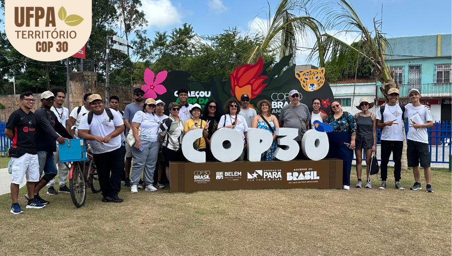 Fotografia posada de um grupo de pessoas atrás de um letreiro da COP 30. Sobre a foto, um selo identifica: UFPA TERRITÓRIO DA COP.