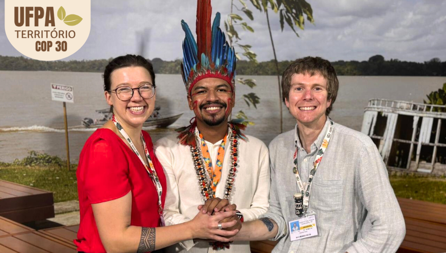 Fotografia posada destaca o estudante indígena Tel Guajajara, acompanhado por outras duas pessoas. Todos sorriem. Tel usa cocar e colares indígenas. Sobre a foto, um selo identifica: UFPA TERRITÓRIO DA COP.