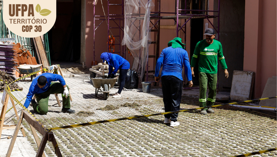 Fotografia registra um grupo de trabalhadores da construação civil em ação. Há um carro de mão e andaimes na imagem. Sobre a foto, um selo identifica: UFPA TERRITÓRIO DA COP.