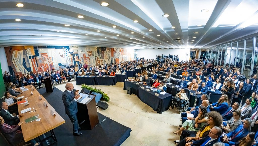 Fotografia registra uma sala cheia, com as pessoas atentas à apresentação do presidente da república, Luís Inácio da Silva.