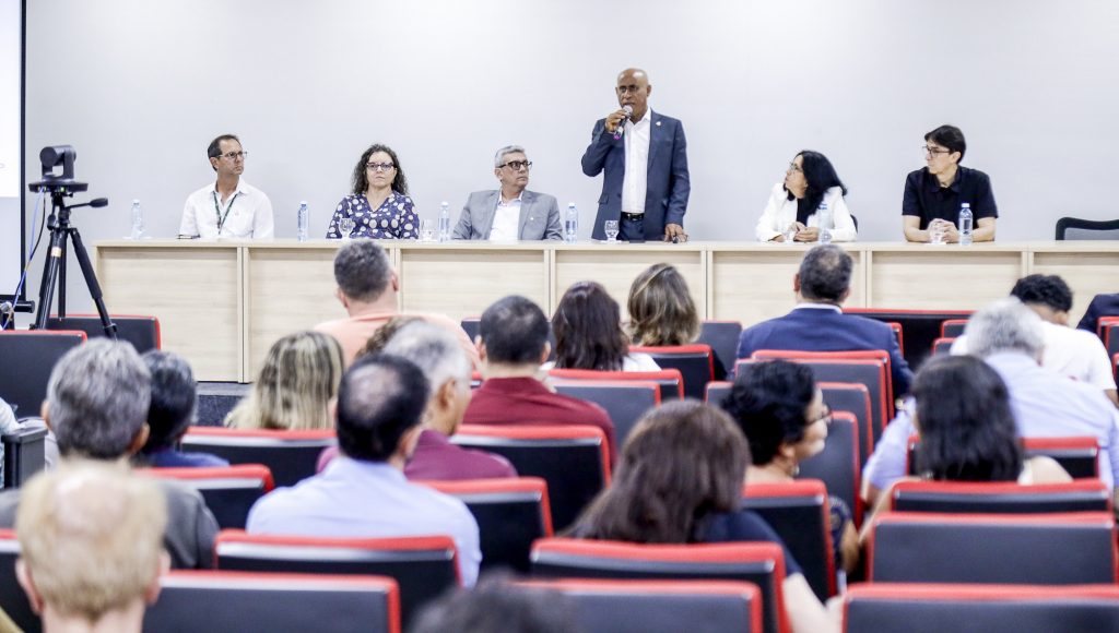 Fotografia registra a mesa de um evento. Nela estão presentes o reitor da UFPA, Gilmar Pereira da Silva; a pró-reitora de Pesquisa e Pós-graduação, Iracilda Sampaio; e outras quatro pessoas.