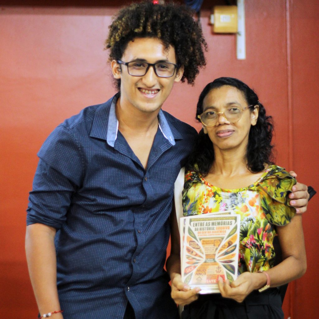 Fotografia posada registra um homem e uma mulher. Os dois sorriem. A mulher segura um exemplar do livro em mãos.