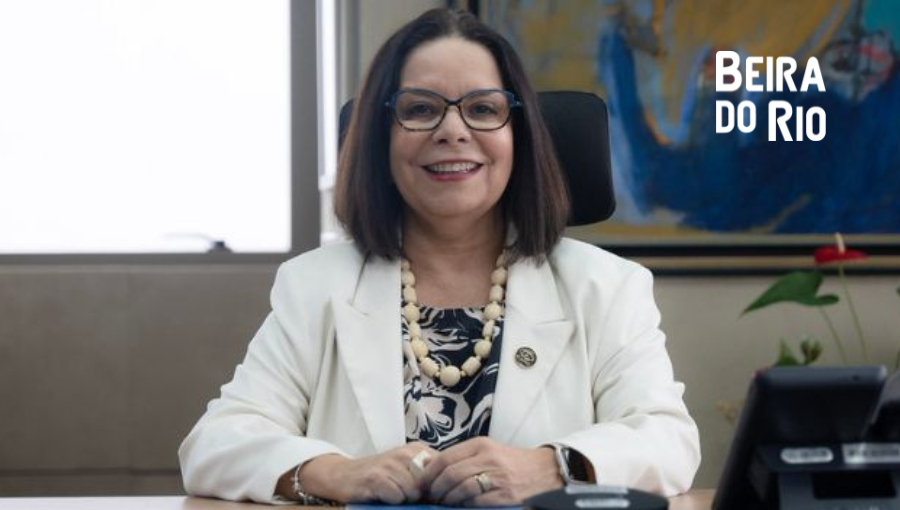 Fotografia posa da presidente da Capes, Denise Pires de Carvalho. Ela sorri, está com os braços apoiados em uma mesa e veste roupas claras. Sobre a foto, a logomarca do Jornal Científico Beira do Rio.