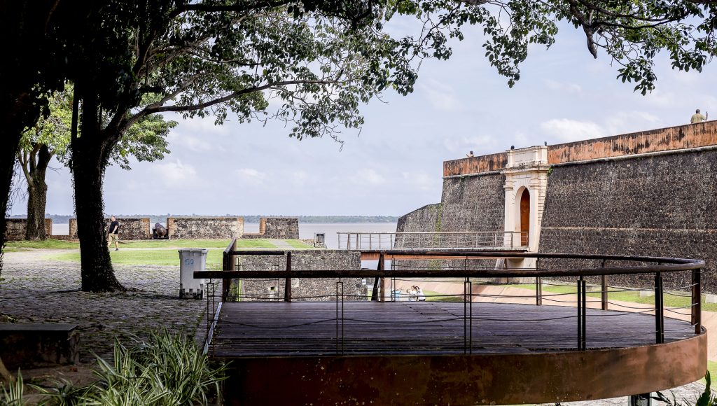 Fotografia registra parte da entrada no Forto do Castelo, em Belém do Pará. A foto registra uma muralha de pedras e um arco no meio dessa muralha.