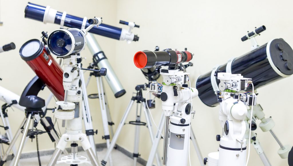 Fotografia registra vários telescópios disposto em um ambiente fechado.