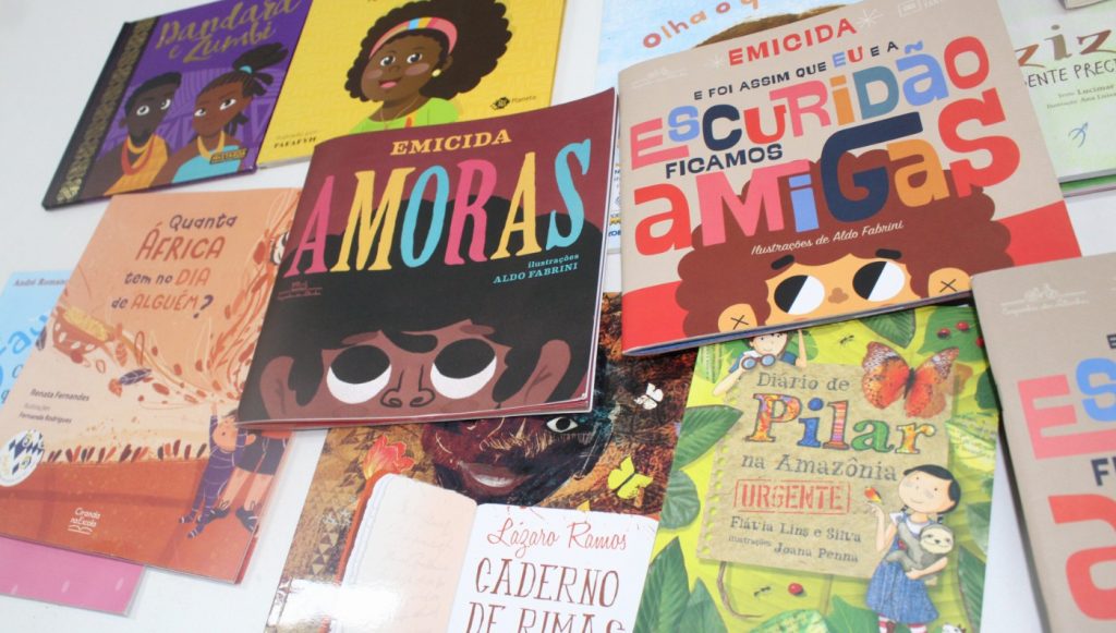 Fotografia registra várias capas de livros dispostas uma ao lado da outra. Algumas das acapas são: Amoras, Quanta África tem no dia de Alguém, E foi assim que eu e a escuridão ficamos amigas, Diário de Pilar na Amazônia, Dandara e Zumbi, entre outras.