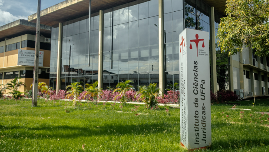 Fotografia da fachada do Instituto de Ciências Jurídicas da UFPA. Em frente, há um totem de identificação do prédio em um jardim com gramado.