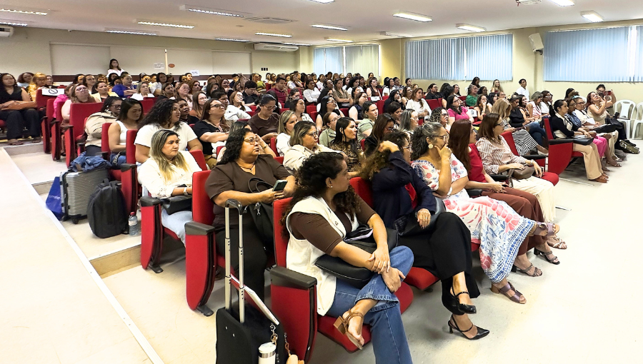 Fotografia registra a plateia de um auditório. O auditório está com todas as cadeiras ocupadas.