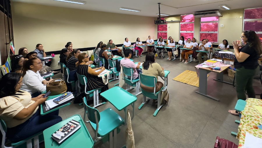Fotografia registra uma sala de aula cheia. Todos são adultos.