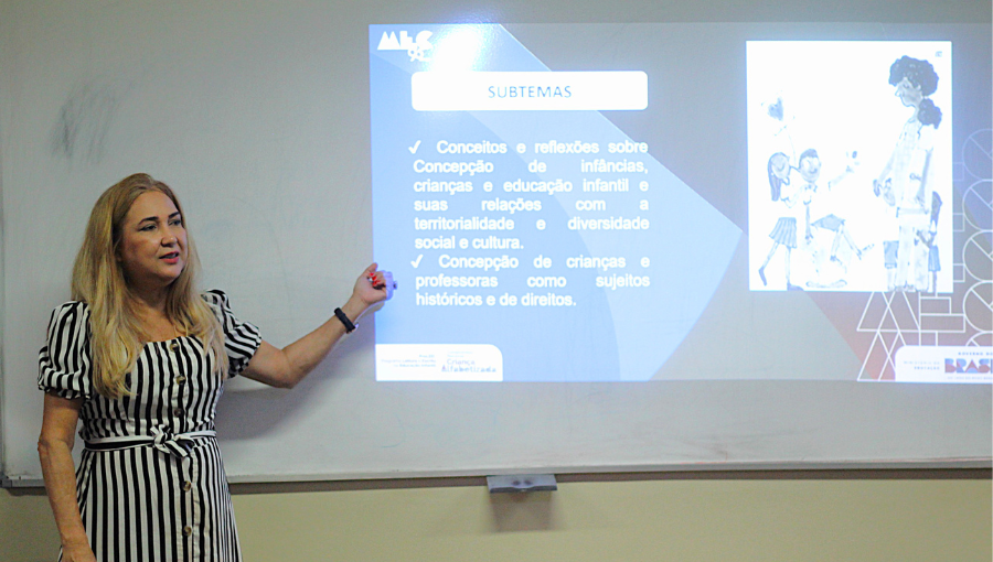 Fotografia registra uma mulher falando ao apontar para uma projeção em um quadro branco. A projeção tem a logo do MEC.