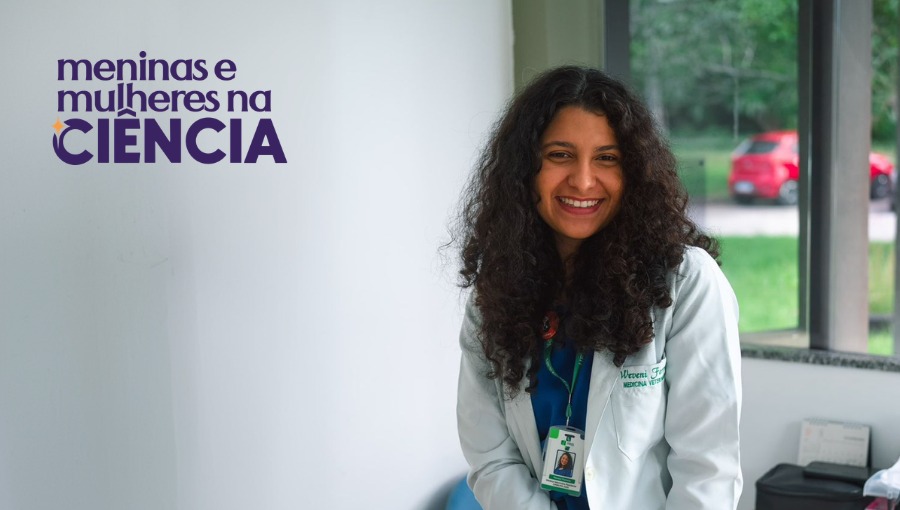 Fotografia mostra jovem de cabelos longos e soltos, vestindo um jaleco e sentada na ponta de uma mesa.