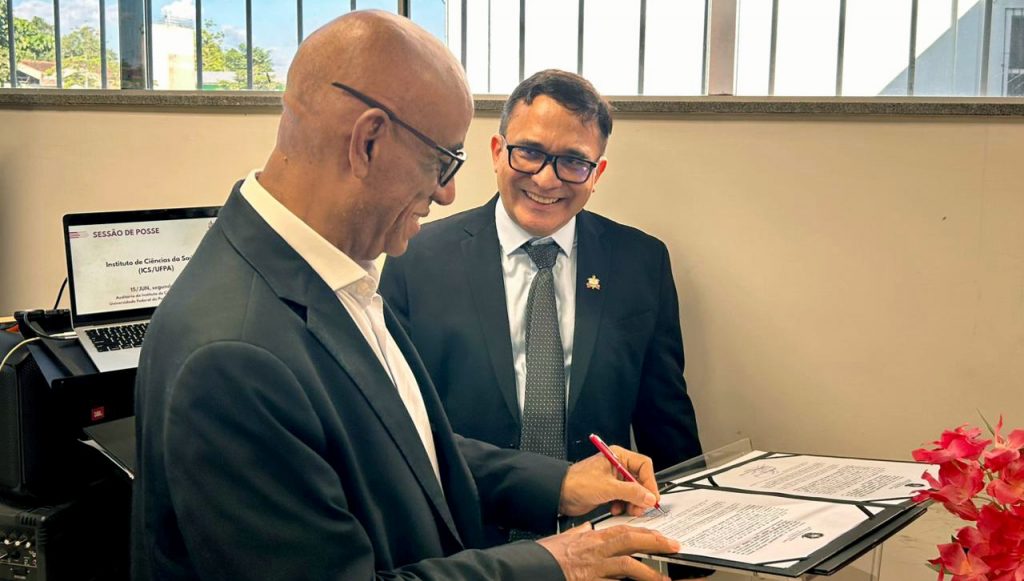 Fotografia registra o reitor da UFPA, Gilmar Pereira da Silva, assinado um documento, sendo observado pelo coordenador-geral do ICS, professor Carlomagno Bahia.