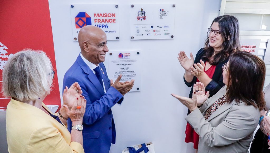 Fotografia registra um grupo de quatro pessoas em frente a placa escrito "Maison France UFPA". As pessoas aplaudem. Entre as pessoas está o reitor da UFPA, Gilmar Pereira da Silva.
