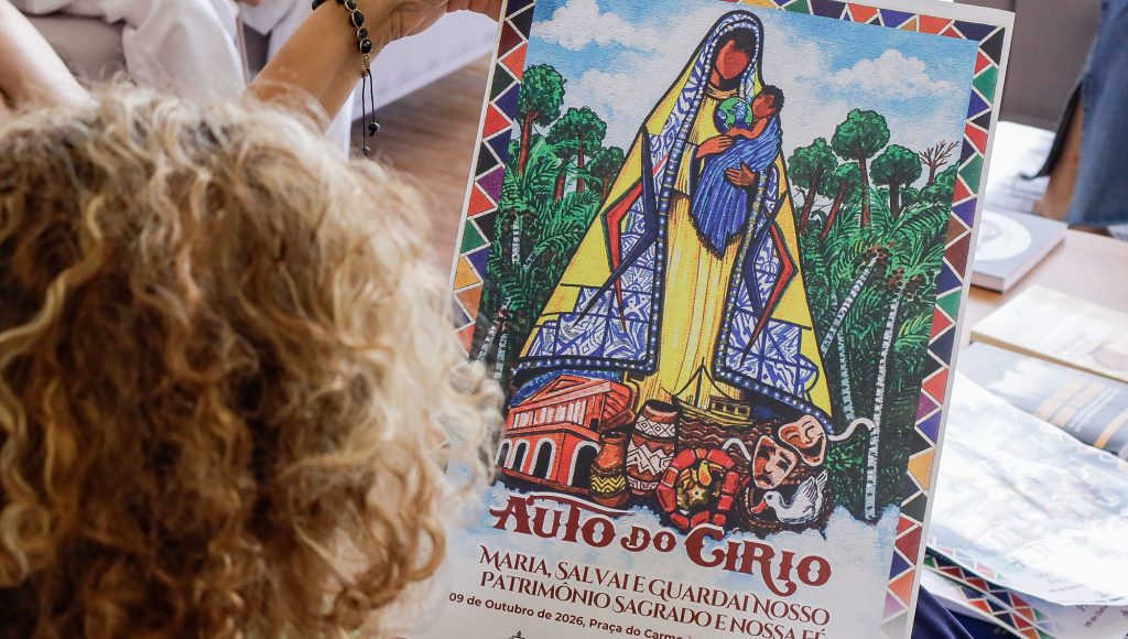 Fotografia registra uma pessoa segurando o cartaz do Auto do Círio 2026. No cartaz é possível ver uma imagem que remete à Nossa Senhora de Nazaré. Ao fundo, o desenho de árvores. A frente da imagem, os desenhos de cerâmicas com motivos marajoaras, máscaras de teatro, pato de miriti, cobra de miriti e o Teatro da Paz. Abaixo dos desenhos, a chamada "Auto do Círio".