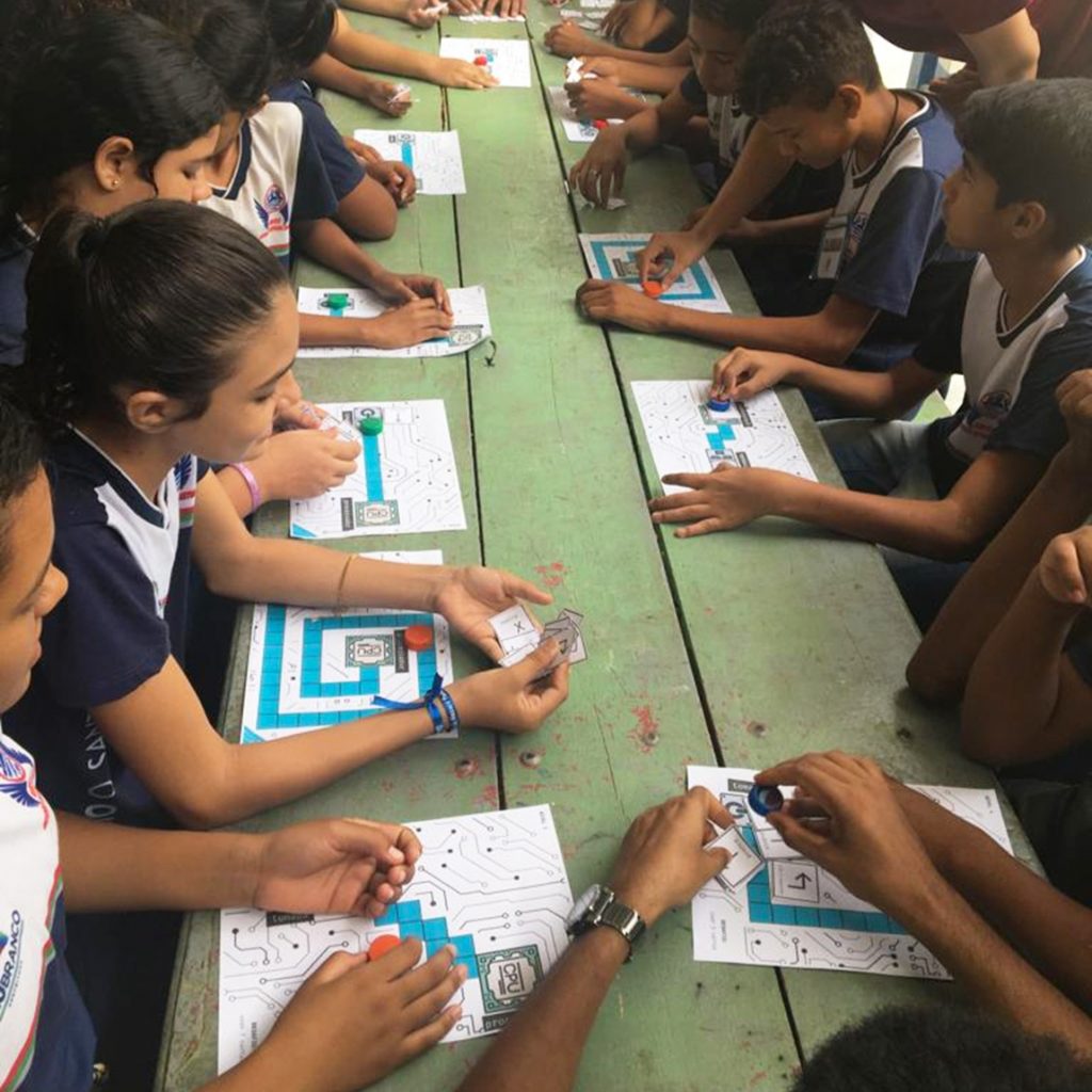 FOTOGRAFIA REGISTRA UM GRUPO DE CRIANÇAS JOGANDO COM CARDS E DESENHOS EM FOLHAS.