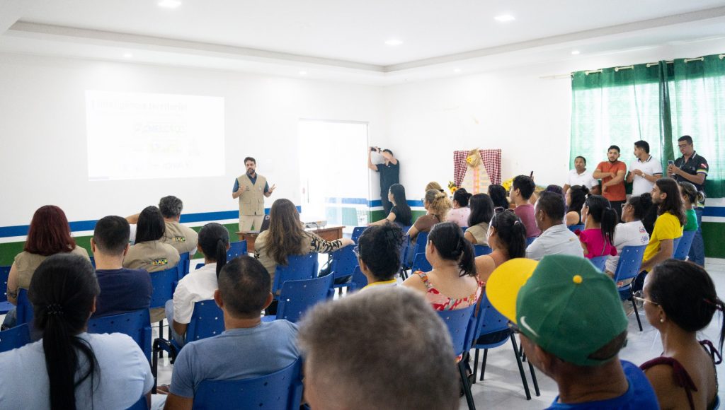 Fotografia registra um homem falando para uma grande plateia, que está disposta em uma sala.