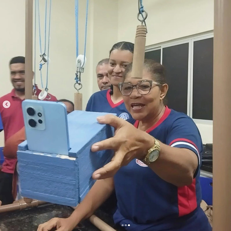 Fotografia registra uma mulher manuseando uma caixa que contém um telefone celular. A caixa está pendurada em uma estrutura feita de canos PVC.