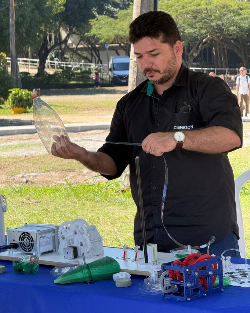 Fotografia registra o professor Wellington manuseando garrafas pets, em uma máquina.