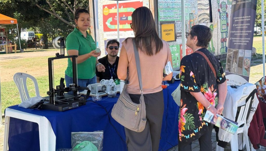 Fotografia registra um grupo de pessoas sob uma tenda. De um lado, uma homem e uma mulher falam e gesticulam.