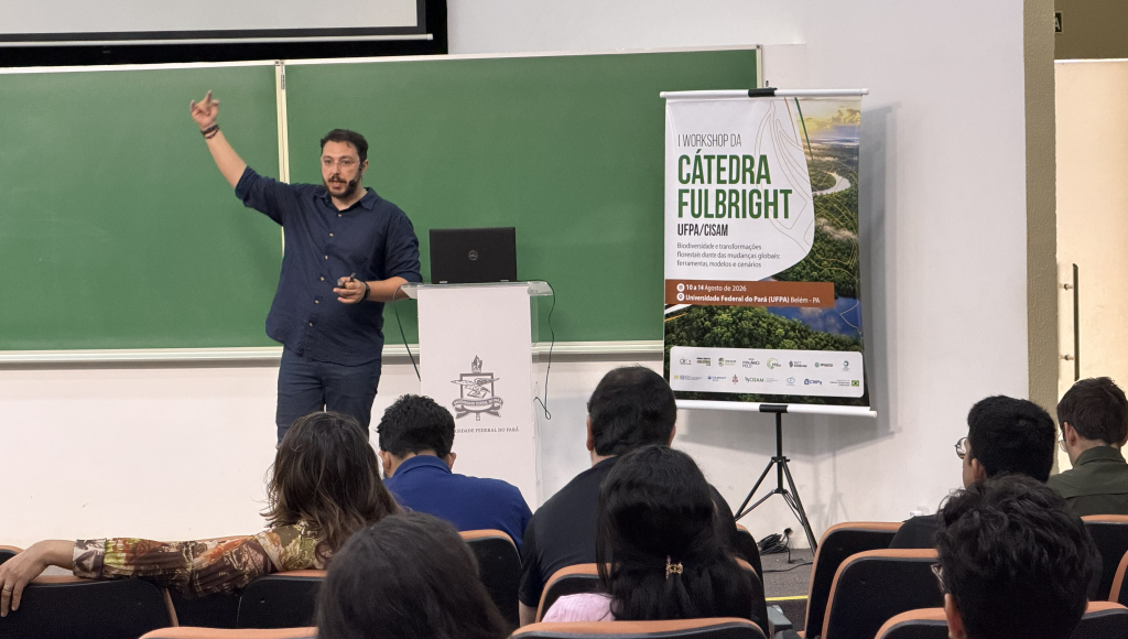 fOTYOGRAFIA REGISTRA UM HOMEM FALANDO AO LADO DE UM BANNER DA CÁTEDRA FULBRIGHT.
