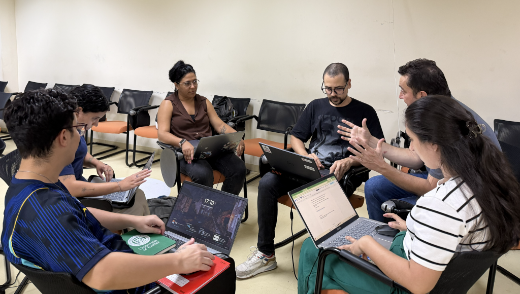 FOTOGRAFIA UM GRUPO DE PESSOAS CONVERSANDO. TODOS ESTÃO SENTADAS EM CADEIRAS DISPOSTAS EM UM CÍRCULO.