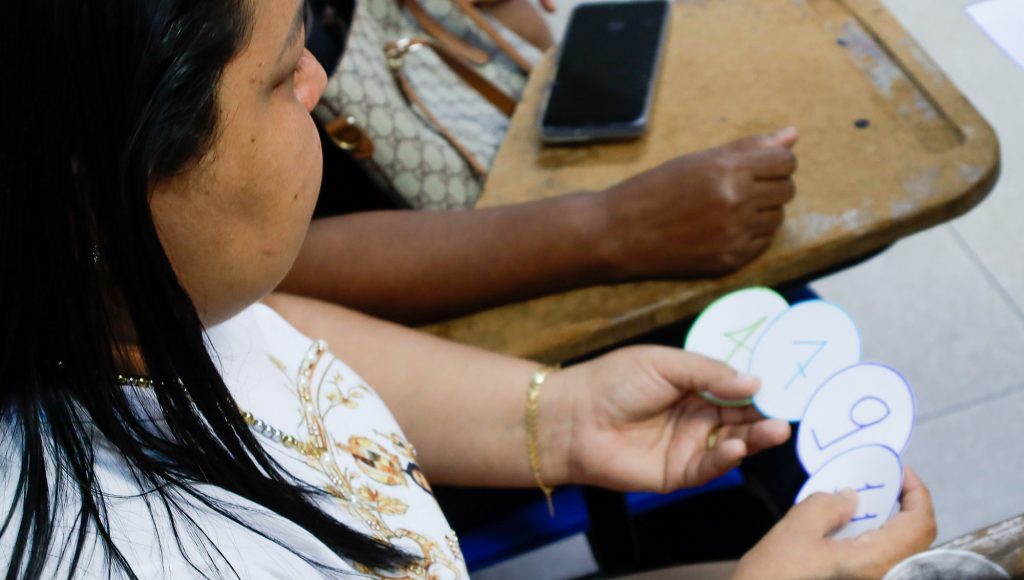 Fotografia registra as mãos de uma pessoas manuseando círculos de papeis com números desenhados.