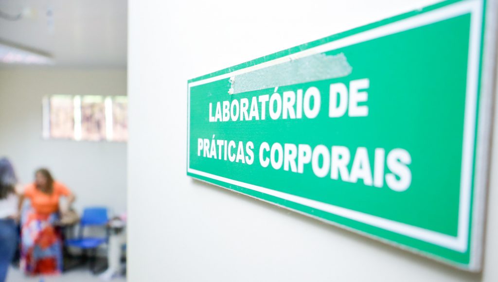 Fotografia registra a placa de uma porta: LABORATÓRIO DE PRÁTICAS CORPORAIS.