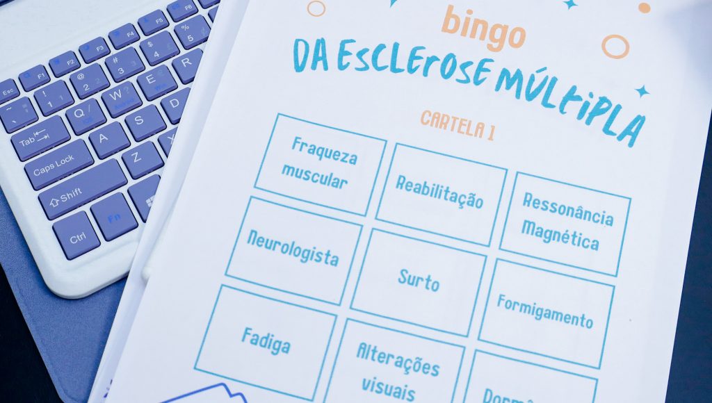 Fotografia de uma cartela de bingo que, no lugar dos números, destaca os seguintes sintomas: fraqueza muscular, reabilitação, ressonância magnética, neurologista, surto, formigamento, fadiga e alterações visuais.