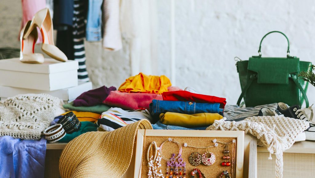 Fotografia registra uma mesa com vários produtos expostos: blusas, bolsa e brincos.