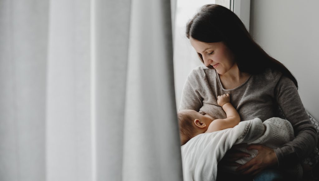 Fotografia registra uma mulher segurando um bebê no colo. Ele mama.