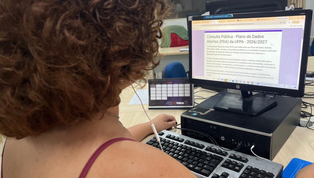 Fotografia registra parte do corpo de uma pessoa que está em frente a um computador de mesa. Na tela do computador, há uma formulário aberto com o seguinte título: consulta pública Plano de Dados Abertos (PDA) da UFPA 2026/2027.