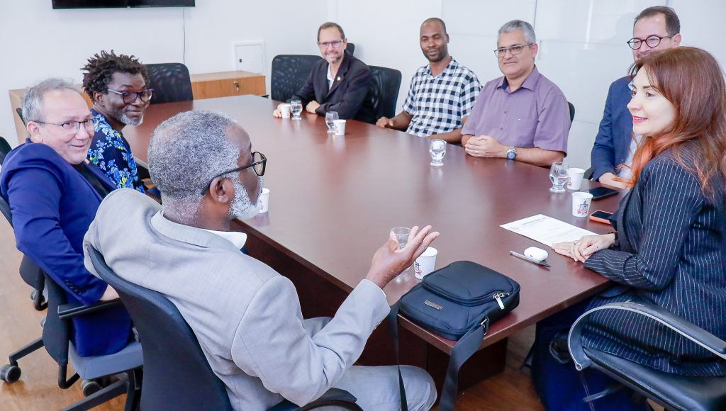Fotografia registra um grupo de pessoas sentado ao redor de uma mesa em uma sala fechada. Entre o grupo estão a vice-reitora da UFPA, Loiane Prado, e o professor catedrático da UniLuanda Alfredo Gabriel Buza.